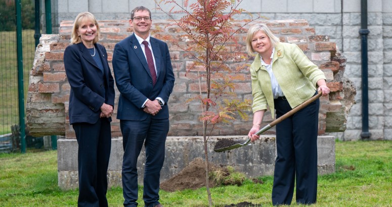 Alex Plant, Deirdre Michie and Provost Judy Whyte Three people smiling after planting a tree in the green grass infront of concrete building