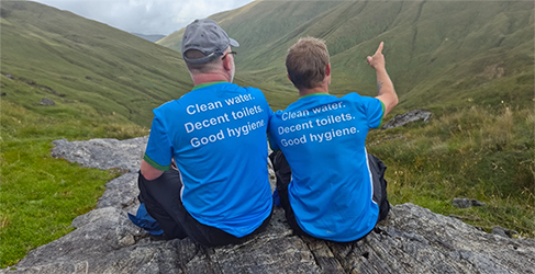 Munro Challenge 2024 complete Two climbers from the back looking up at CisteDhubh munro wearing WaterAid Tshirts with Clean Water, Decent toilets, Good hygiene printed on the back