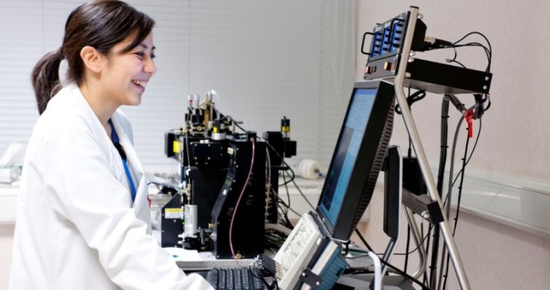 Scientist in lab coat using a laptop with advanced laboratory equipment in the background. Scientist in lab coat using a laptop with advanced laboratory equipment in the background.
