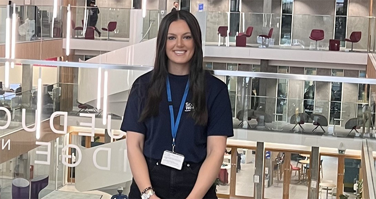 Apprenticeship Week Holly Henderson Trainee Manager Holly Henderson in front of a glass awards cabinet promoting Apprenticeship Week